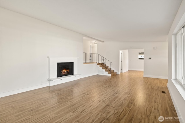 1003 9th St NW, Puyallup, WA 98371 - unfurnished living room featuring wood finished floors, a lit fireplace, stairs, and healthy amount of natural light