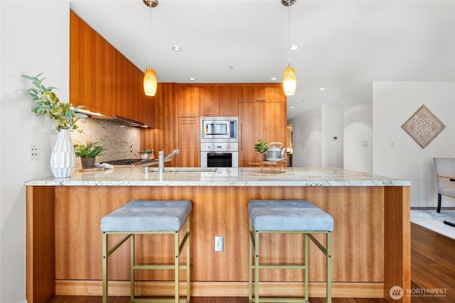 10700 NE 4th St Unit 806, Bellevue, WA 98004 - kitchen featuring appliances with stainless steel finishes, brown cabinets, a peninsula, decorative backsplash, and hanging light fixtures
