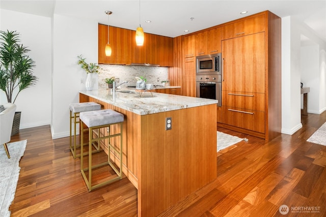 10700 NE 4th St Unit 806, Bellevue, WA 98004 - kitchen with appliances with stainless steel finishes, brown cabinetry, a peninsula, dark wood-style flooring, and recessed lighting