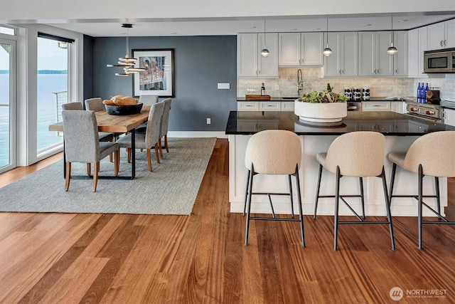 3717 Beach Dr SW Unit 207, Seattle, WA 98116 - kitchen featuring stainless steel microwave, dark countertops, wood finished floors, and tasteful backsplash