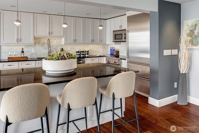 3717 Beach Dr SW Unit 207, Seattle, WA 98116 - kitchen featuring appliances with stainless steel finishes, dark wood-type flooring, backsplash, a kitchen bar, and white cabinetry