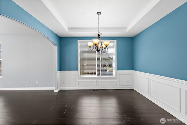 1208 Goldfinch Ave SW, Orting, WA 98360 - unfurnished dining area featuring a raised ceiling, a chandelier, arched walkways, dark wood-style floors, and wainscoting