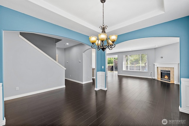 1208 Goldfinch Ave SW, Orting, WA 98360 - unfurnished living room with arched walkways, a chandelier, a tiled fireplace, a tray ceiling, and wood finished floors