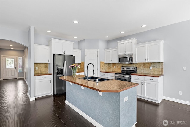 1208 Goldfinch Ave SW, Orting, WA 98360 - kitchen with stainless steel appliances, arched walkways, dark wood finished floors, white cabinets, and recessed lighting