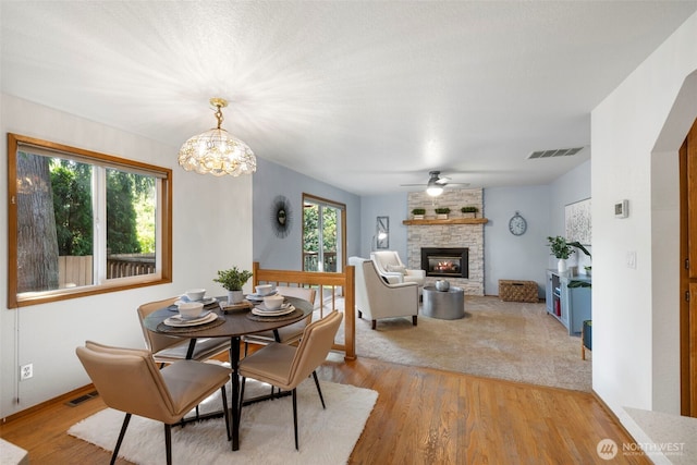 3905 109th Pl SE, Everett, WA 98208 - dining space with light wood-type flooring, a stone fireplace, a chandelier, and a ceiling fan
