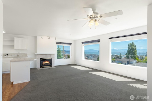 910 34th St Unit 302, Anacortes, WA 98221 - unfurnished living room featuring a tiled fireplace, a ceiling fan, baseboards, and a sink