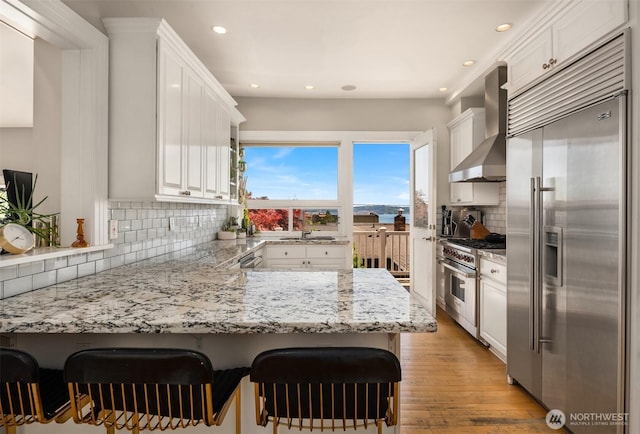 1012 2nd Ave W, Seattle, WA 98119 - kitchen featuring premium appliances, wall chimney exhaust hood, recessed lighting, white cabinetry, and backsplash