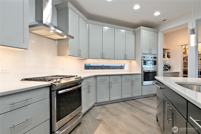 3359 Terry Ln, Enumclaw, WA 98022 - kitchen featuring appliances with stainless steel finishes, wall chimney range hood, gray cabinets, light wood-style flooring, and decorative backsplash