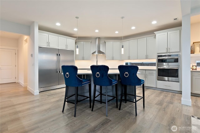 3359 Terry Ln, Enumclaw, WA 98022 - kitchen featuring stainless steel appliances, wall chimney exhaust hood, light wood-type flooring, a kitchen island, and light countertops