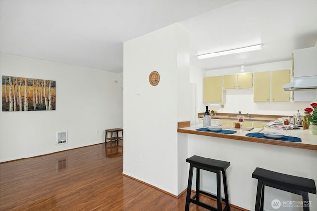 12613 SE 42nd St Unit 613, Bellevue, WA 98006 - kitchen with under cabinet range hood, dark wood-style floors, cream cabinetry, and a kitchen breakfast bar