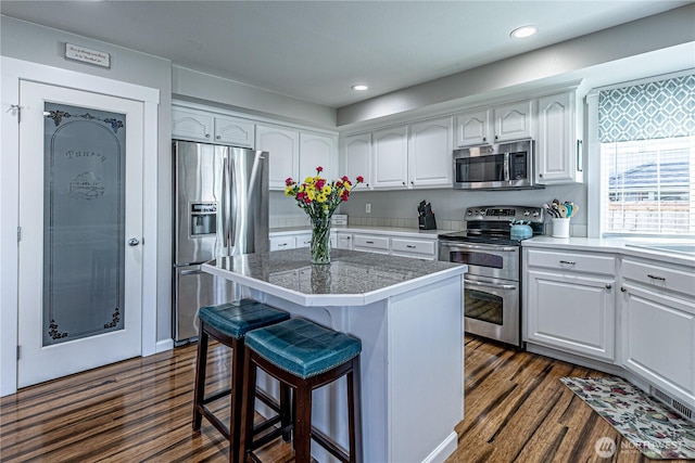 17716 25th Ave E, Tacoma, WA 98445 - kitchen with stainless steel appliances, white cabinets, a kitchen island, a kitchen bar, and dark wood-type flooring