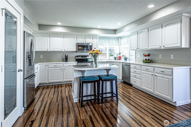 17716 25th Ave E, Tacoma, WA 98445 - kitchen with appliances with stainless steel finishes, white cabinets, a kitchen bar, dark wood-type flooring, and light countertops