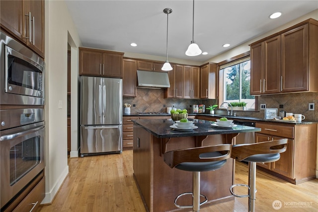 13020 112th Ave NE, Kirkland, WA 98034 - kitchen featuring stainless steel appliances, under cabinet range hood, light wood-type flooring, a kitchen bar, and recessed lighting