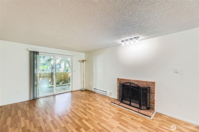 921 130th St SW Unit E102, Everett, WA 98204 - unfurnished living room featuring a baseboard heating unit, light wood-style floors, a textured ceiling, and a fireplace