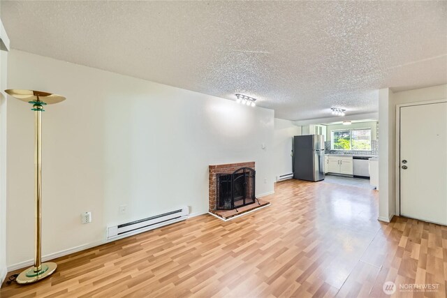 921 130th St SW Unit E102, Everett, WA 98204 - unfurnished living room featuring a baseboard heating unit, light wood-style floors, a textured ceiling, and a fireplace