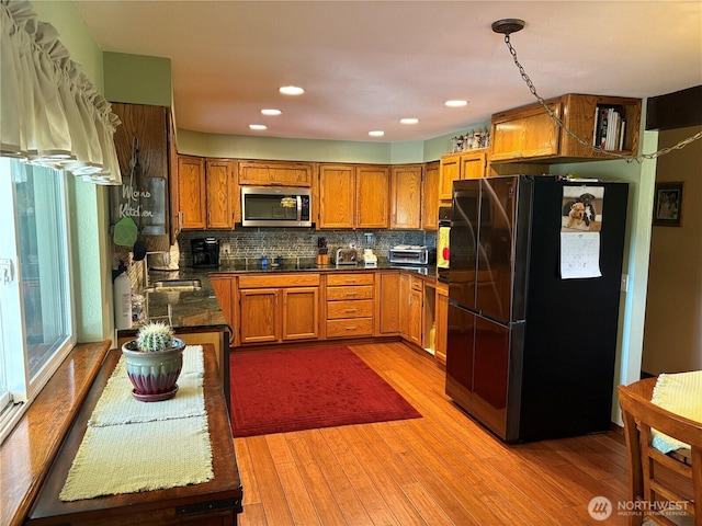 301 Main St, Riverside, WA 98849 - kitchen featuring freestanding refrigerator, stainless steel microwave, brown cabinets, dark countertops, and light wood-style flooring