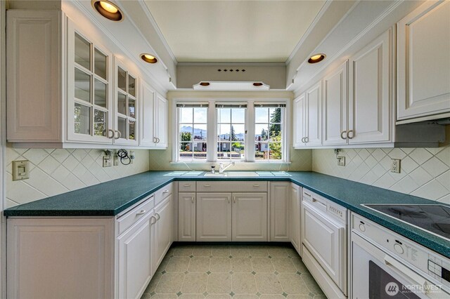 1415 E 2nd St, Port Angeles, WA 98362 - kitchen with dark countertops, decorative backsplash, white cabinets, glass insert cabinets, and white oven