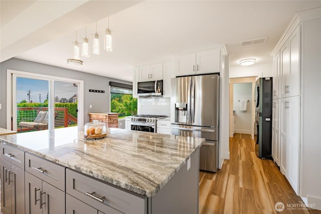 2483 Hilltop Rd, Ferndale, WA 98248 - kitchen with appliances with stainless steel finishes, light wood-type flooring, a center island, light stone countertops, and backsplash
