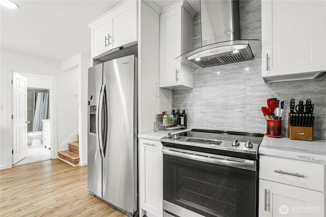 8739 17th Ave NW, Seattle, WA 98117 - kitchen featuring stainless steel appliances, wall chimney range hood, backsplash, white cabinets, and light wood-style floors