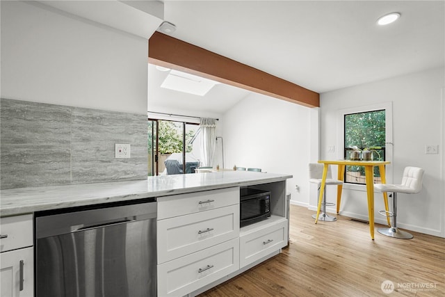 8739 17th Ave NW, Seattle, WA 98117 - kitchen with stainless steel dishwasher, black microwave, a skylight, light stone counters, and white cabinets