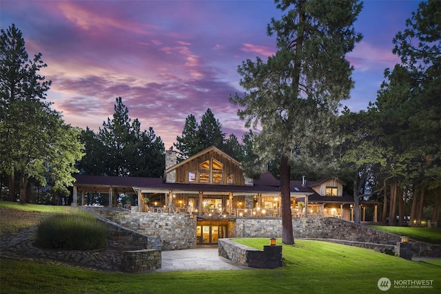 6286 Five Mile Rd, The Dalles, OR 98058 - back of property at dusk with a yard, stone siding, a patio, and a chimney