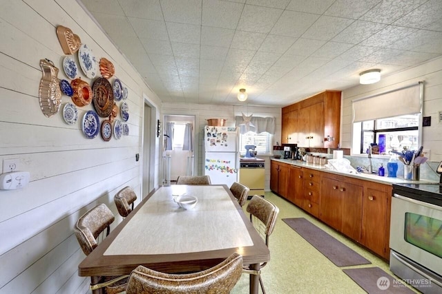 1215 199th Pl, Long Beach, WA 98631 - kitchen featuring freestanding refrigerator, stainless steel electric range oven, brown cabinets, light countertops, and wood walls