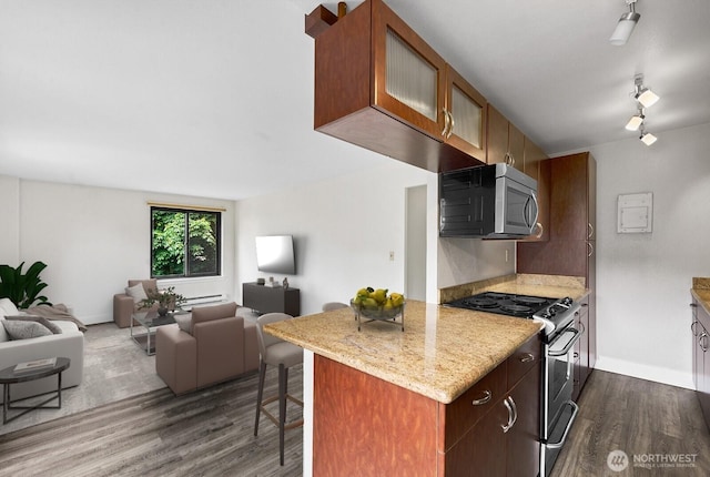 1105 Spring St Unit 407, Seattle, WA 98104 - kitchen featuring appliances with stainless steel finishes, dark wood finished floors, a breakfast bar area, open floor plan, and light stone countertops