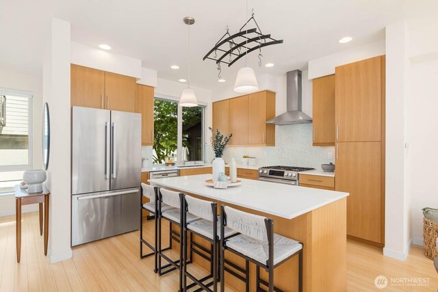 5175 42nd Ave S, Seattle, WA 98118 - kitchen featuring stainless steel appliances, wall chimney exhaust hood, a kitchen bar, light wood-style flooring, and backsplash