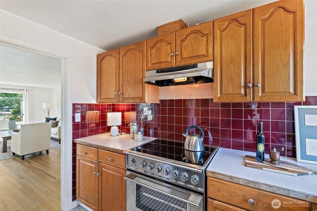 4603 15th Ave S, Seattle, WA 98108 - kitchen featuring under cabinet range hood, stainless steel electric stove, light wood-type flooring, brown cabinetry, and decorative backsplash