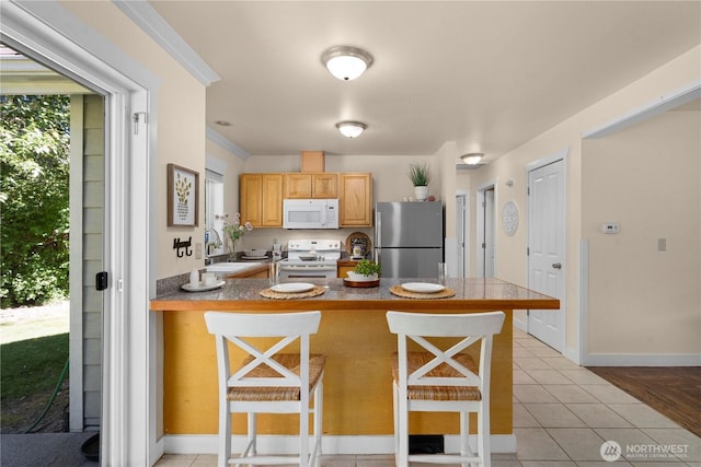 2502 218th St E, Spanaway, WA 98387 - kitchen featuring white appliances, a peninsula, a kitchen bar, light tile patterned floors, and light brown cabinetry