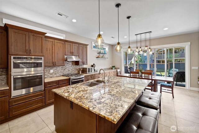 1132 121st St E, Tacoma, WA 98445 - kitchen with stainless steel appliances, light tile patterned flooring, decorative backsplash, under cabinet range hood, and a kitchen bar