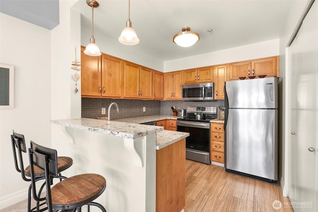 910 Harris Ave Unit 304, Bellingham, WA 98225 - kitchen with stainless steel appliances, a peninsula, tasteful backsplash, a breakfast bar, and brown cabinetry