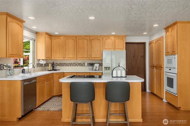 9119 185th Pl SW, Edmonds, WA 98026 - kitchen featuring white appliances, light wood-style flooring, a textured ceiling, a kitchen island, and a breakfast bar area