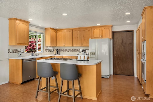 9119 185th Pl SW, Edmonds, WA 98026 - kitchen with appliances with stainless steel finishes, light wood-type flooring, a textured ceiling, a center island, and a breakfast bar area