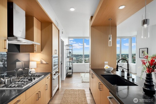 1321 Seneca St Unit 1001, Seattle, WA 98101 - kitchen with wall chimney range hood, stainless steel appliances, light wood-style flooring, decorative light fixtures, and dark stone counters