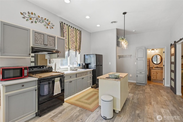 7322 NE Blue Goose Rd, Moses Lake, WA 98837 - kitchen with black appliances, under cabinet range hood, gray cabinets, a barn door, and light wood-style floors