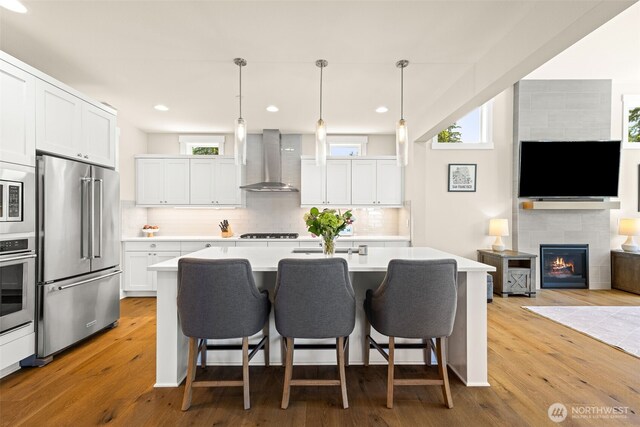 8704 188th St SW, Edmonds, WA 98026 - kitchen with appliances with stainless steel finishes, wall chimney exhaust hood, decorative backsplash, light countertops, and light wood finished floors