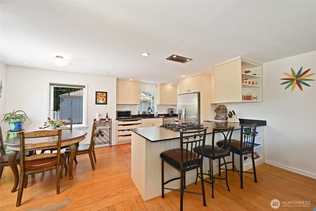 9539 49th Ave NE, Seattle, WA 98115 - kitchen featuring appliances with stainless steel finishes, a peninsula, light wood finished floors, a breakfast bar area, and dark countertops