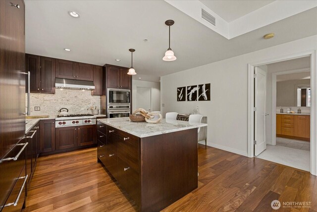 10700 NE 4th St Unit 712, Bellevue, WA 98004 - kitchen featuring appliances with stainless steel finishes, under cabinet range hood, dark wood-style floors, a center island, and backsplash