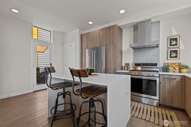 1100 14th Ave, Seattle, WA 98122 - kitchen featuring stainless steel appliances, wall chimney exhaust hood, a kitchen breakfast bar, wood finished floors, and recessed lighting