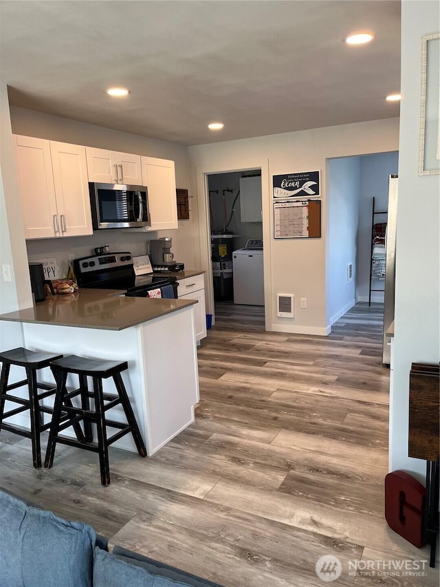916 35th St, Anacortes, WA 98221 - kitchen featuring stainless steel microwave, range with electric cooktop, washer / clothes dryer, white cabinets, and a peninsula