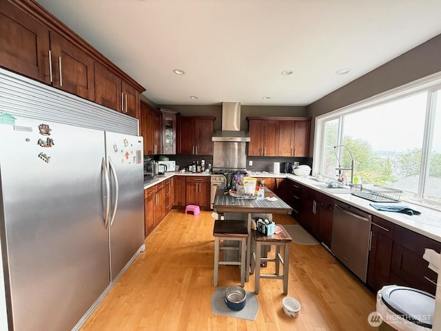9844 Arrowsmith Ave S, Seattle, WA 98118 - kitchen with appliances with stainless steel finishes, wall chimney range hood, light countertops, light wood-style floors, and decorative backsplash