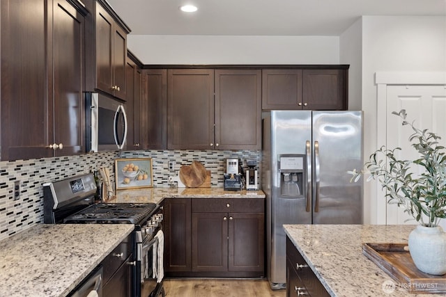 3119 13th Avenue Ct NW, Puyallup, WA 98371 - kitchen with stainless steel appliances, dark brown cabinets, light wood-type flooring, light stone countertops, and decorative backsplash