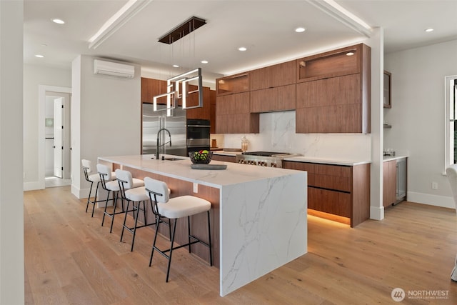 11888 SE 5th St, Bellevue, WA 98005 - kitchen featuring modern cabinets, an AC wall unit, brown cabinets, appliances with stainless steel finishes, and a kitchen breakfast bar