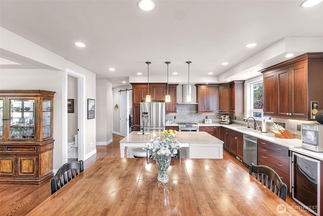 1301 Broad St, Bellingham, WA 98229 - kitchen featuring stainless steel appliances, wall chimney range hood, light countertops, an island with sink, and tasteful backsplash