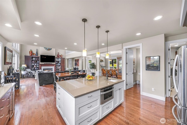 1301 Broad St, Bellingham, WA 98229 - kitchen featuring stainless steel appliances, open floor plan, a kitchen island with sink, a warm lit fireplace, and white cabinetry