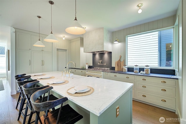 9208 11th Ave NW, Seattle, WA 98117 - kitchen featuring light wood-style floors, a breakfast bar, premium range hood, an island with sink, and decorative light fixtures