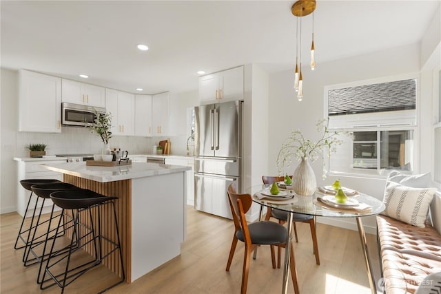 12852 Occidental Ave S, Seattle, WA 98168 - kitchen featuring stainless steel appliances, tasteful backsplash, a breakfast bar, a center island, and light wood-style flooring