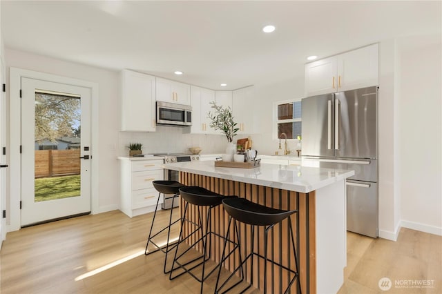 12852 Occidental Ave S, Seattle, WA 98168 - kitchen featuring stainless steel appliances, light wood-style flooring, a kitchen breakfast bar, a kitchen island, and tasteful backsplash