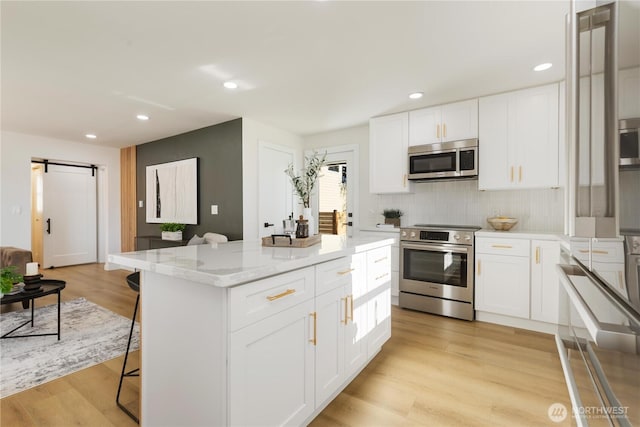12852 Occidental Ave S, Seattle, WA 98168 - kitchen featuring appliances with stainless steel finishes, a barn door, a kitchen breakfast bar, backsplash, and light stone countertops